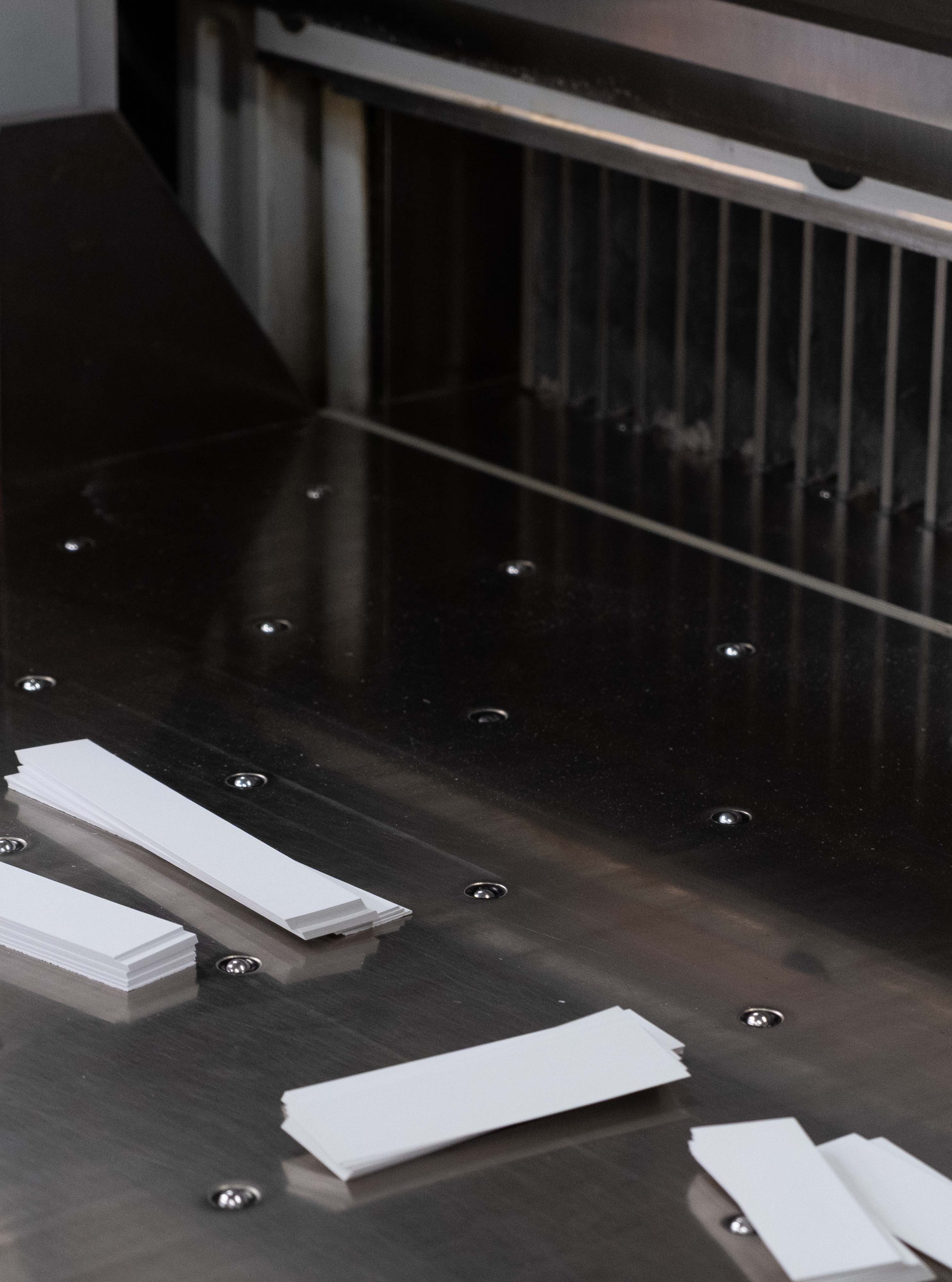 Freshly cut white cards resting on a paper cutting machine.